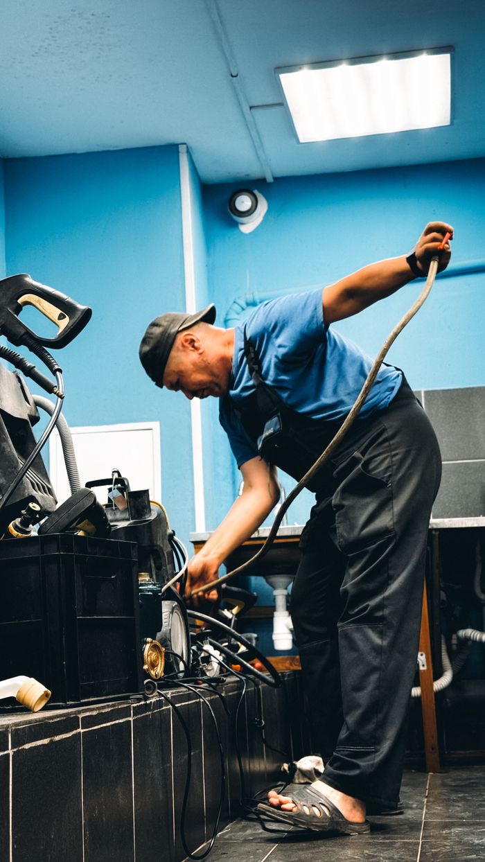 about-02 A technician in blue attire repairing equipment in an indoor workshop setting.